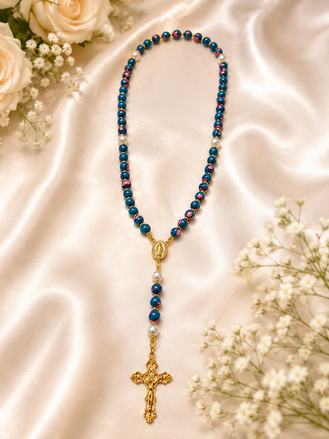 Handcrafted blue and pink marbled rosary displayed on champagne satin with ivory roses and baby's breath